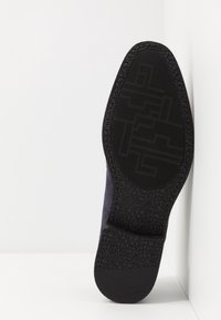 Semelle noire en caoutchouc avec un motif de grip texturé, talon légèrement surélevé et arrière renforcé. Matériau sombre et doux sur la partie supérieure.