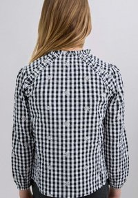Blusa de cuadros en blanco y negro con acentos florales bordados, cuello con volantes y mangas abullonadas. La vista trasera muestra el detalle del escote.