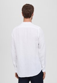 Camicia bianca a maniche lunghe in lino, con orlo dritto e polsini abbottonati, con colletto semplice e senza motivi visibili.