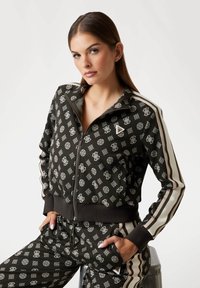 Black zip-up track jacket featuring a repeating light-colored pattern, striped sleeves, and a ribbed hem and cuffs. Paired with matching pants.