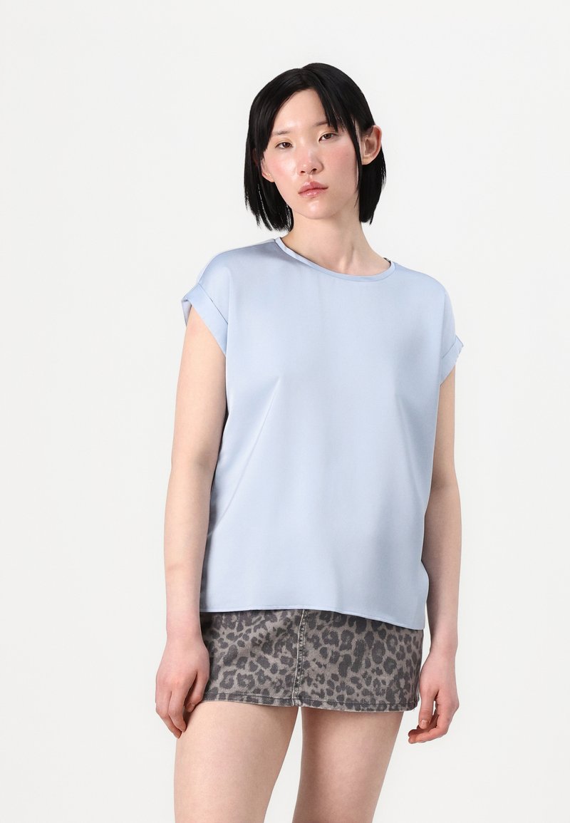 Blusa azzurra chiara a maniche corte con scollo rotondo, dal tessuto morbido e dalla vestibilità rilassata, abbinata a una gonna di jeans grigia con stampa leopardata.