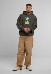 Felpa grigia con una grafica che presenta un globo e il testo "Market Studios", abbinata a pantaloni beige a vestibilità comoda e sneakers chiare.