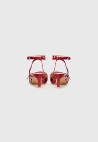 Red patent leather high-heeled sandals with ankle straps and a curved block heel. Smooth finish, open back, and minimalistic design.