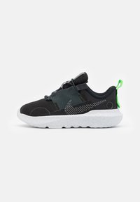 Black athletic shoe with mesh upper, grey accents, and a white speckled sole. Features green pull tab and textured patterns on the side.