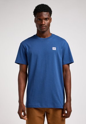 T-shirt en coton bleu à manches courtes avec un col rond, présentant un petit patch logo Lee sur la poitrine gauche. Design simple et coupe régulière.