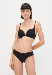 Soutien-gorge en dentelle noire et culotte assortie avec des bords festonnés ; bonnets lisses et motif délicat ; bretelles réglables ; quincaillerie minimale.