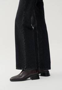Black wide-leg jeans with a raw hem, paired with dark brown ankle boots featuring a square toe and low block heel.