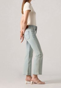 Jeans en denim bleu clair avec une coupe droite, taille haute et poches arrière, associés à un haut crème à manches courtes en côtes et des sandales à talons blanches.