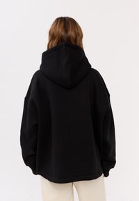 Zwarte hoodie met een losse pasvorm, verlaagde schouderlijnen en een zachte textuur; heeft een grote capuchon en subtiele stikdetails.