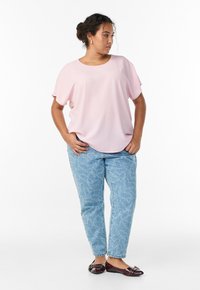 Svetloružový top s voľným strihom a krátkymi rukávmi, v kombinácii so svetlomodrými džínsami s motívom srdiečok. Nosené s tmavými plochými topánkami.