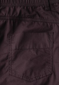 Tissu violet foncé des shorts avec une taille élastique. Comprend une poche arrière carrée avec des coutures visibles. Texture lisse.