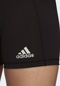 Pantalones cortos deportivos negros hechos de tejido elástico, con el logo blanco de "adidas", costuras planas y textura suave.