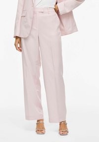 Pantalon large rose pâle avec une coupe ajustée, doté d'un devant plat, de poches latérales et d'une texture lisse, associé à des sandales argentées.