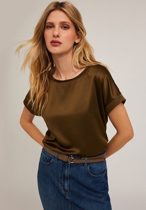Top satin verde oliva scuro con maniche corte arrotolate, abbinato a una gonna di denim e una cintura marrone, che mette in mostra una texture liscia e lucida.