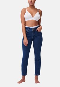 Bralette bianco con spalline regolabili abbinato a jeans in denim blu scuro a vita alta. I jeans presentano una chiusura con bottone e un design aderente.