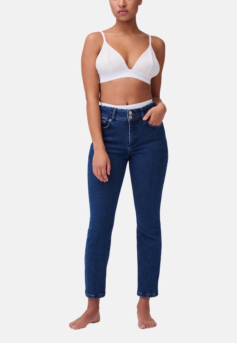 Bralette bianco con spalline regolabili abbinato a jeans in denim blu scuro a vita alta. I jeans presentano una chiusura con bottone e un design aderente.