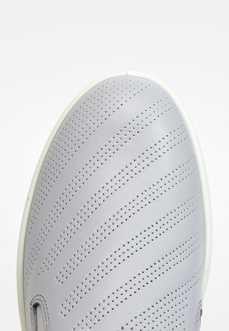 Grauer Lederschuh mit durchbrochenen Streifen, runder Zehenpartie und weißer Sohle. Besitzt eine weiche Textur und ein minimalistisches Design.
