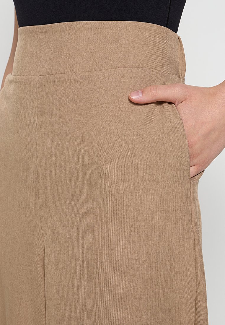 Beige hoge taillebroek met een gladde textuur, voorzien van zijkleppen en een getailleerde pasvorm. De stof lijkt lichtgewicht en luchtig.