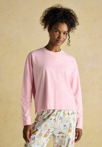 Svetlo roza bombažna majica z dolgimi rokavi in sproščenim krojem ter okroglim izrezom, v kompletu s pajama hlačami s vzorcem, ki prikazujejo različne ilustracije psov.