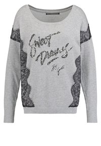 Sweatshirt gris à manches longues, avec des inserts en dentelle noire et un texte en sequins "Sweet Dreams" sur le devant. ourlet et encolure côtelés.