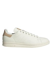 White canvas sneakers with a textured surface, beige heel tab, six eyelets, and a rubber sole; features subtle perforated branding.