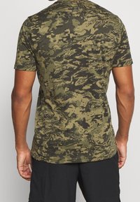 Camiseta de manga corta verde de camuflaje hecha de una tela suave, con un patrón pixelado y un cuello redondeado. Texturas detalladas visibles.