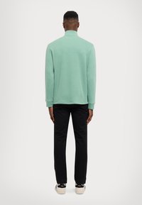 Mintgrön långärmad polo skjorta med hög krage och avslappnad passform, i kombination med svarta slim-fit byxor och ljusa sneakers.