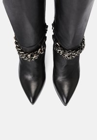 Mustat nahka nilkkurit, joissa on terävät varpaat ja koristeellinen hopeaketju varressa. Silkkinen pinta ja tyylikäs muotoilu.