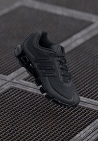 Fekete atlétikai cipő, texturált hálós és szintetikus anyagból készült, fűzős kialakítással, három oldalsó csíkkal és jellegzetes talppal.