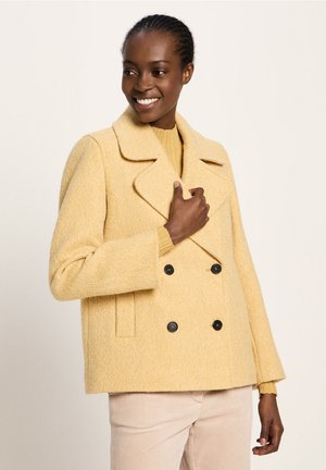 Yellow wool blend double-breasted coat with large lapels, two black buttons, and side pockets. Ribbed mustard sweater underneath.