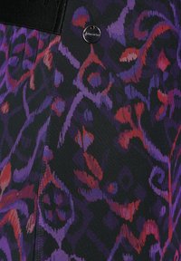 Texturerad tyg med en svart bakgrund och ett färgglatt abstrakt mönster i lila, röd och blå ton; inkluderar en liten metall-logotyp.