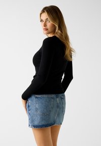 Schwarzes Langarmoberteil kombiniert mit einem hellblauen Denim-Minirock mit Gesäßtaschen, schmaler Passform und rohem Saum.