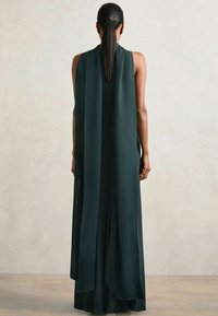 Langes, ärmelloses, dunkelblaugrünes Kleid mit einem fließenden, cape-ähnlichen Rücken; aus glattem, leichtem Stoff gefertigt, der eine schlanke Silhouette erzeugt.