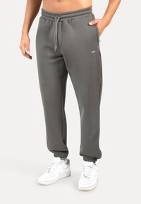 Pantalones deportivos grises con cintura elástica y cordón. Incluyen bolsillos laterales y puños ajustados. Combinados con zapatillas blancas.