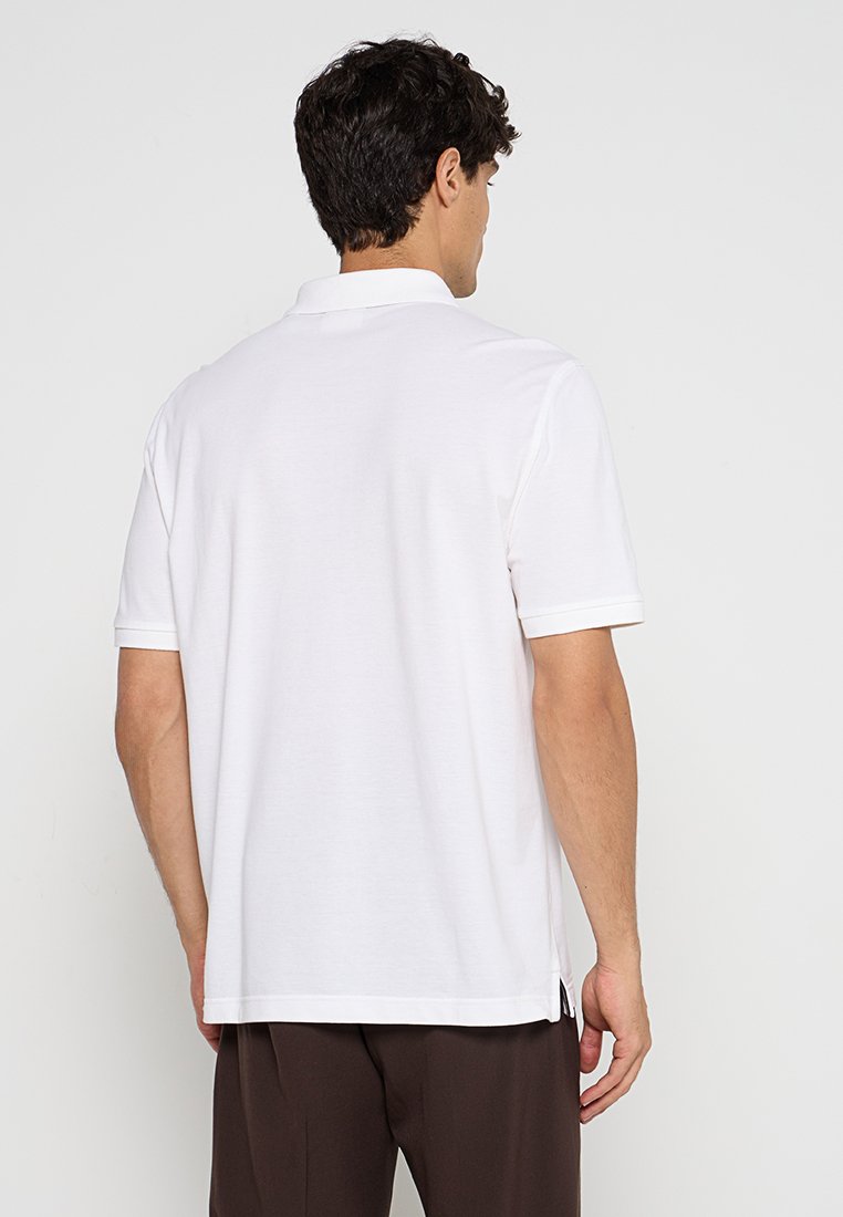 Weißes Poloshirt, kurze Ärmel, weiches Baumwollmaterial, seitliche Schlitze am Saum, klassisches Kragen-Design, schlichte Rückansicht.