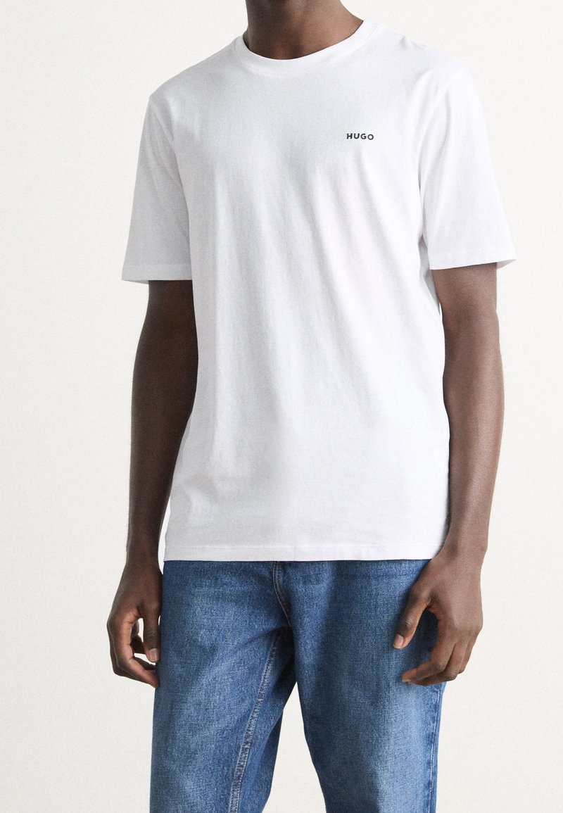 Wit katoenen T-shirt met korte mouwen, met een klein zwart "HUGO" logo op de borst. Gecombineerd met blauwe spijkerbroek. Eenvoudig ontwerp.