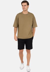 Oversized khaki T-shirt van zachte stof, gecombineerd met zwarte short. Witte sneakers maken de outfit compleet. Eenvoudig en casual ontwerp.