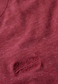 Camiseta marrón en una tela suave y texturizada con un sutil patrón jaspeado. Presenta un logo bordado de "SuperDry" en un color a juego.