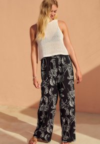 Bílý pletený crop top, černé kalhoty s širokými nohavicemi a bílými listovými vzory, nošené s sandály. Hladká textura, volný střih, ležérní design.