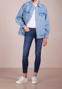 Vaaleansininen farkkutakki, jossa on kauluksellinen kaulus, kaksi rintataskua ja nappikiinnitys, yhdistettynä tummansinihin slim fit -farkkuihin ja valkoisiin tennarit.