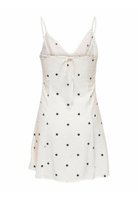 Robe blanche sans manches avec des pois noirs, fines bretelles, un décolleté en V et un détail noué dans le dos.