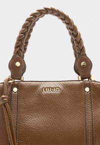 Sac à main en cuir marron avec une poignée tressée, quincaillerie dorée et logo en relief. Texture lisse avec des détails de couture visibles.