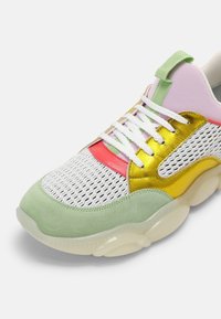 Sneaker multicolore avec une tige en mesh, des accents métalliques dorés et rouges, des superpositions en daim vert, et une semelle translucide épaisse.