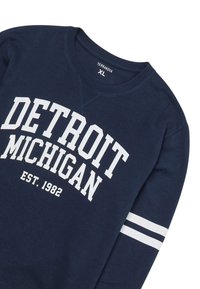 Granatowy sweter z białym napisem "DETROIT MICHIGAN" oraz detalem "EST. 1982". Posiada białe akcenty w paski na rękawach i okrągłym dekolcie.