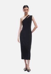 Schwarzes, einseitig geschnittenes Kleid mit einer figura betonten Silhouette, das über silberne Hardware-Details verfügt. Glatte Textur mit einem knielangen Saum.