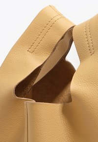 Borsa a mano in pelle gialla con superficie testurizzata, apertura superiore che rivela un interno morbido. Dettagli cuciti visibili lungo i bordi.
