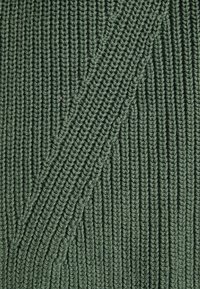 Textured green knitted fabric with vertical ribbing and diagonal accents, showcasing a dense stitch pattern and a soft, natural finish.