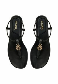 Black flat sandals with a thong design, embellished with a gold floral charm. Features a smooth texture and minimalistic round ankle strap.