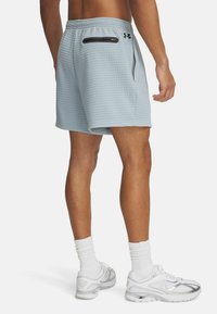 Pantalones cortos de color azul claro con un tejido texturizado, que presentan un bolsillo con cremallera negra en la parte trasera y una cinturilla elástica. Combinados con zapatillas blancas.