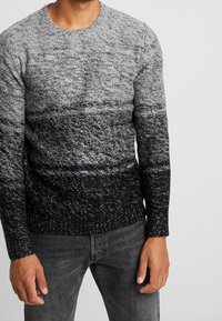 Pull tricot dégradé gris avec un col rond, des poignets et une bande inférieure côtelés, doté d'une finition texturée passant du clair au foncé.